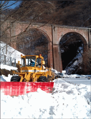 雪の積もった峠道で除雪にあたるホイールローダー